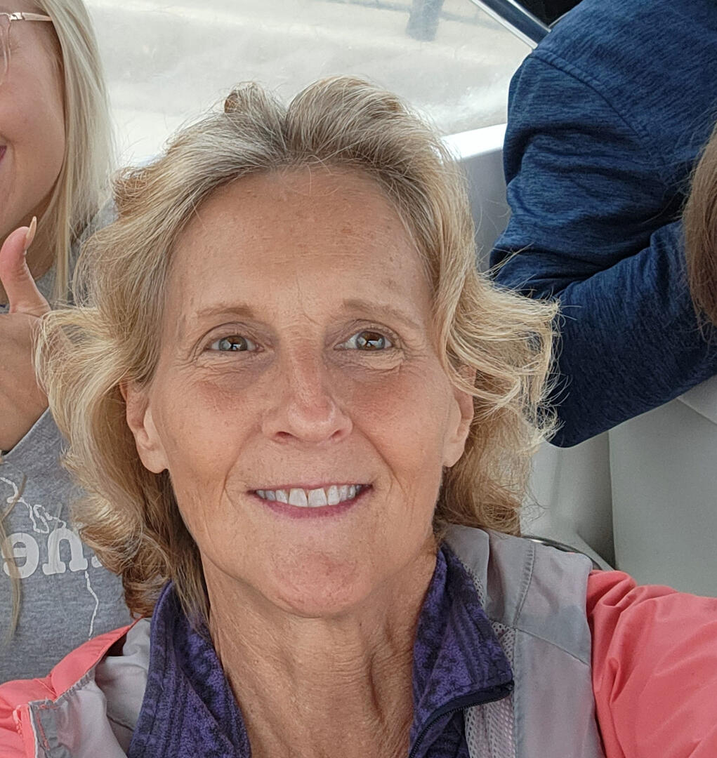 A woman with wavy blonde hair smiling, wearing a gray jacket.