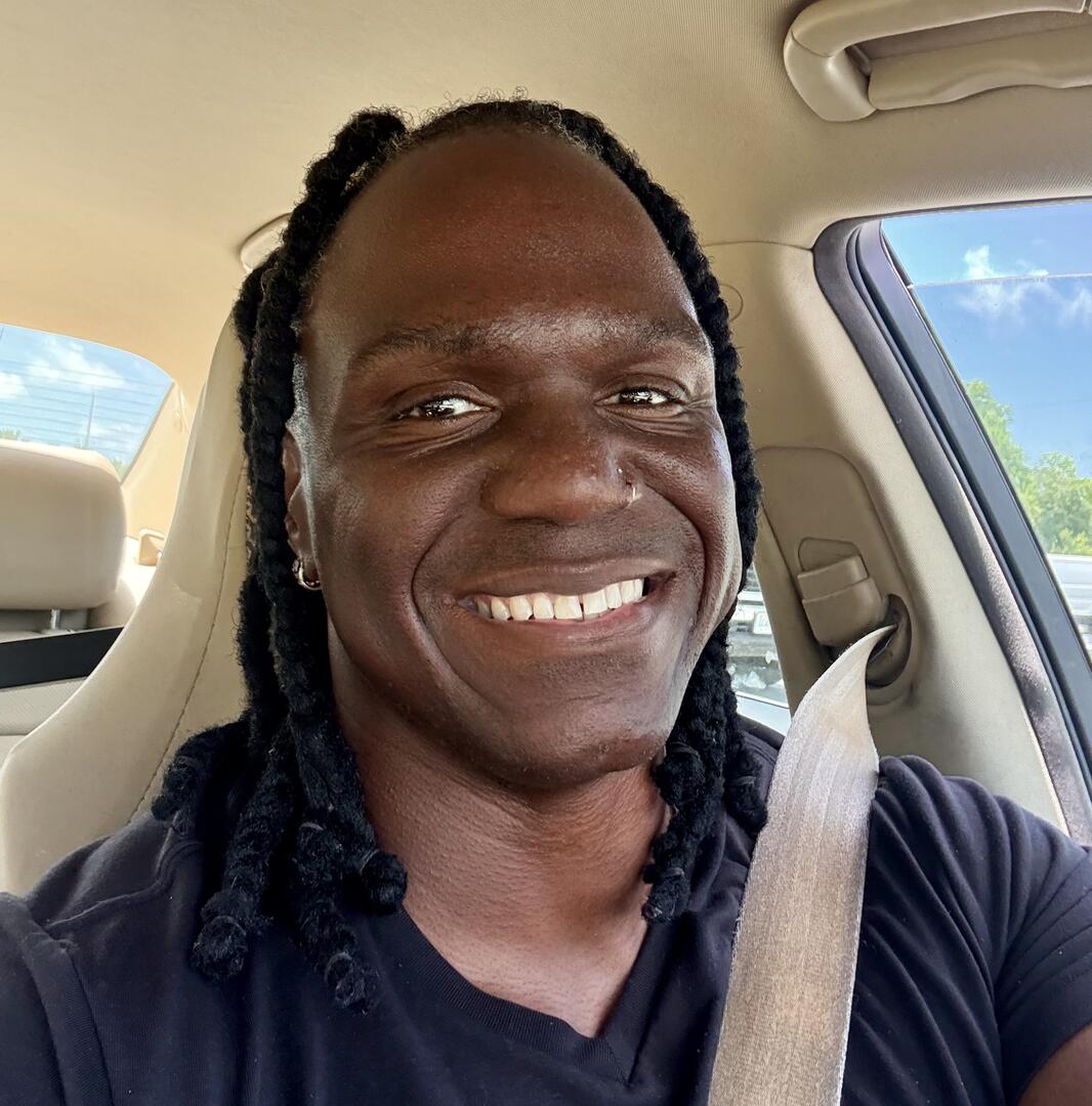 Smiling person with long dark hair driving in a car.